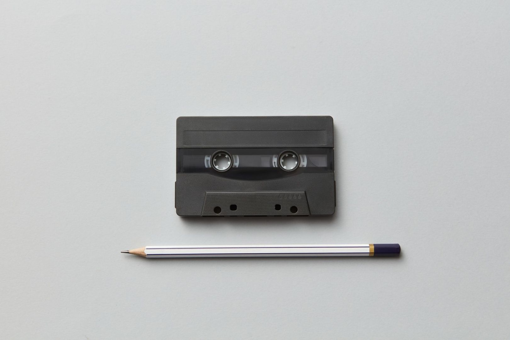 Black audio cassette and pencil arranged on a light gray surface